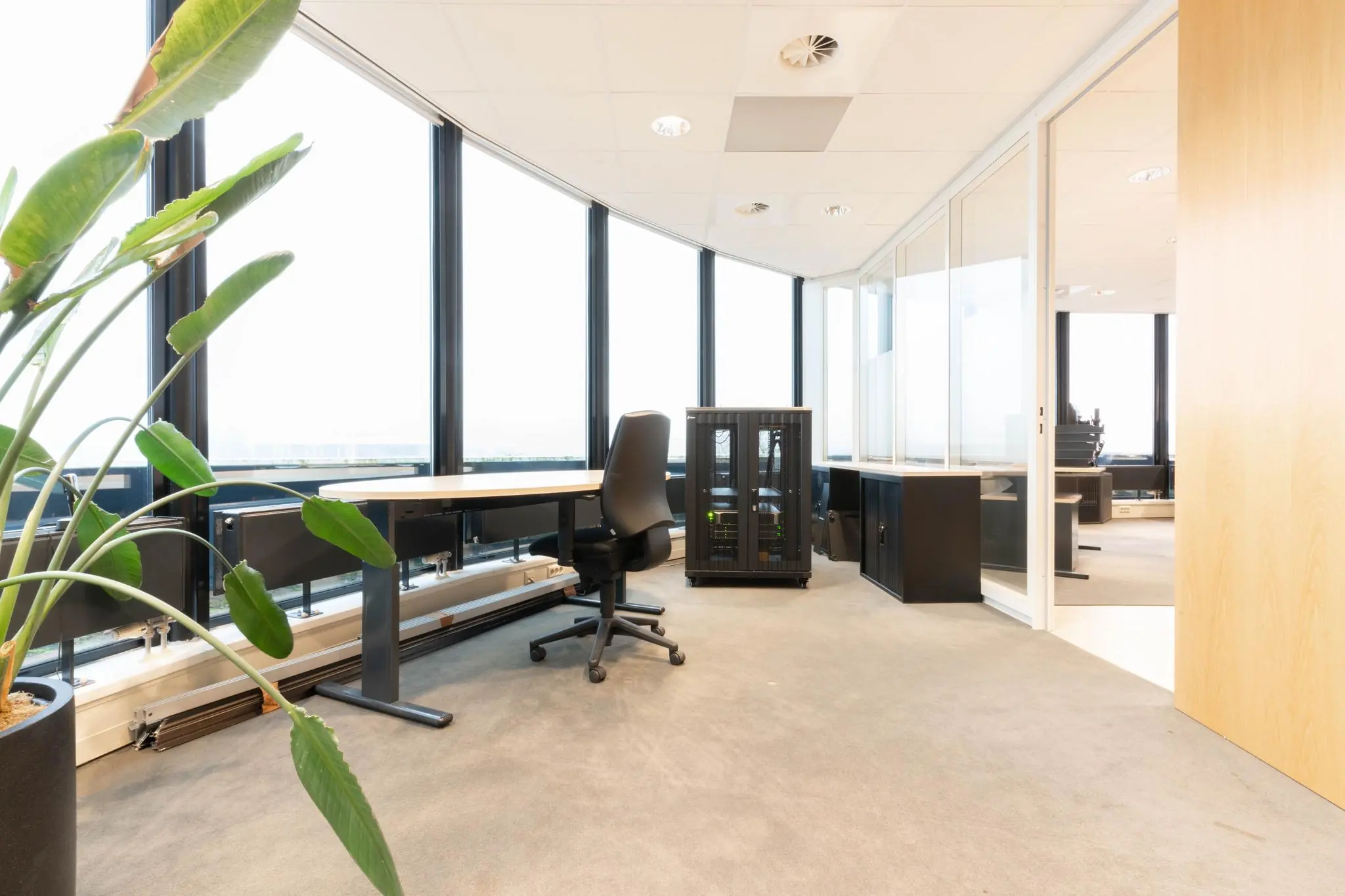 Modern kantoorinterieur aan de 1e Hogeweg met werkplekken, een serverkast en grote raampartijen.